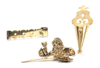Lot 729 - A 19TH CENTURY BRASS AND STEEL ADJUSTABLE HANGING HOOK, A SHAPED CUT-OUT BRASS SPILL HOLDER, A GEORGIAN BRASS SPIT ARM, A CAST LION HEARTH ORNAMENT and A BRASS CAT