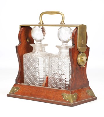 Lot 1138 - A LATE 19TH CENTURY ENGLISH OAK AND BRASS TANTALUS WITH TWO CUT GLASS DECANTERS